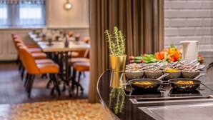 A buffet setup with various dishes and utensils, a decorative plant, and a seating area with tables and chairs. - Cologne Marriott Hotel (Cologne)