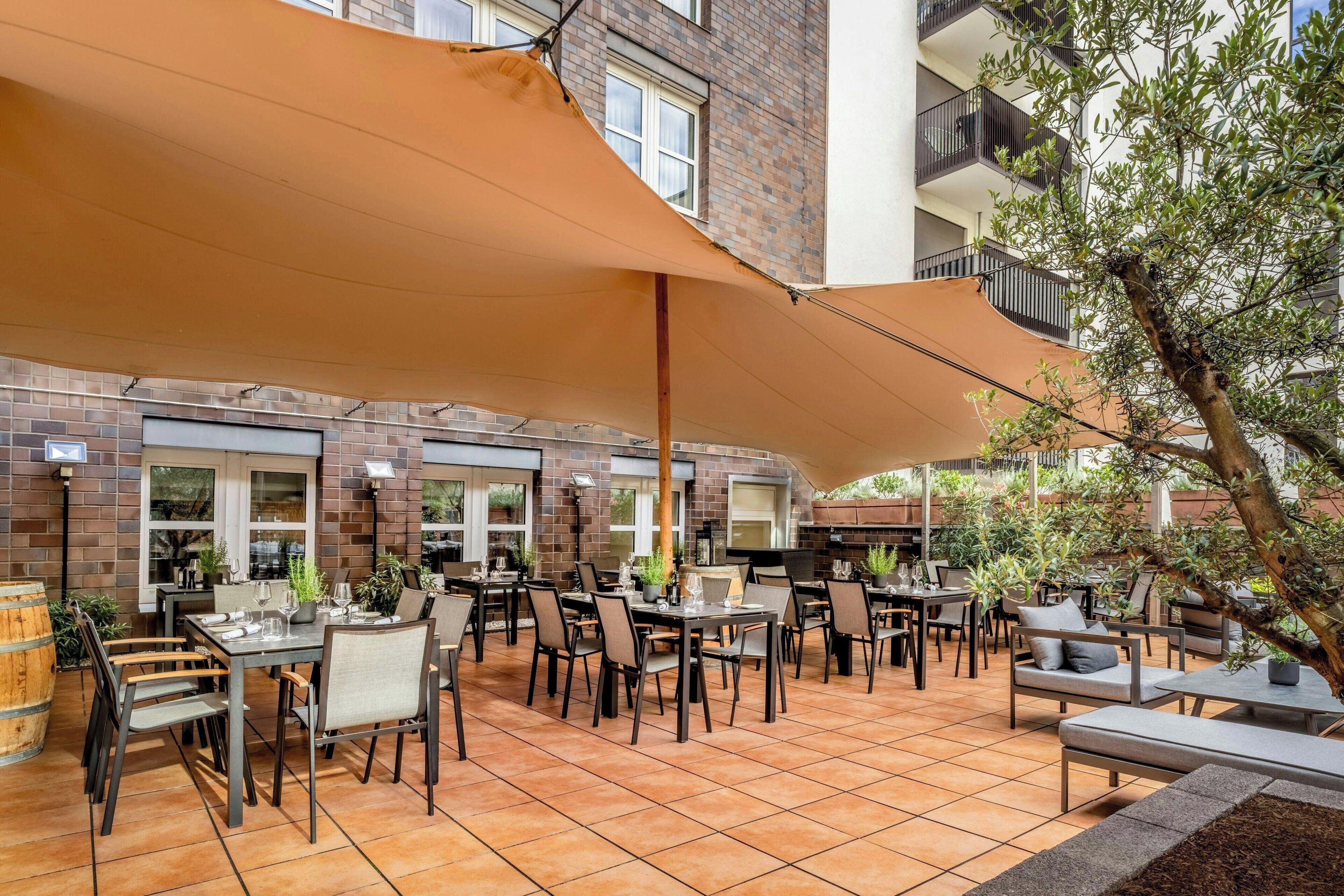 An outdoor patio with multiple tables and chairs, surrounded by brick walls and a large canopy.