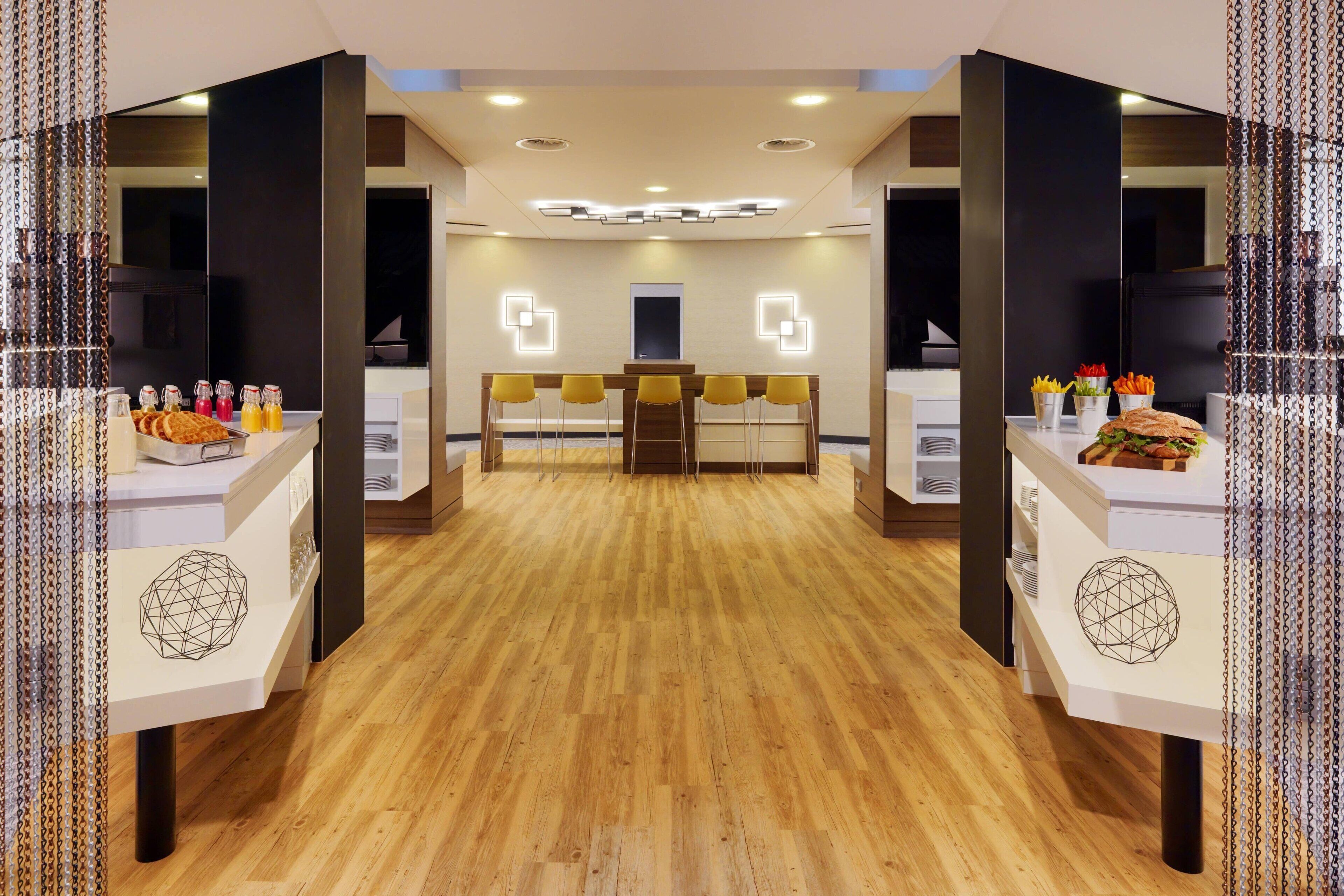 A modern hotel lobby with a wooden floor, a reception desk, and a seating area with yellow chairs.