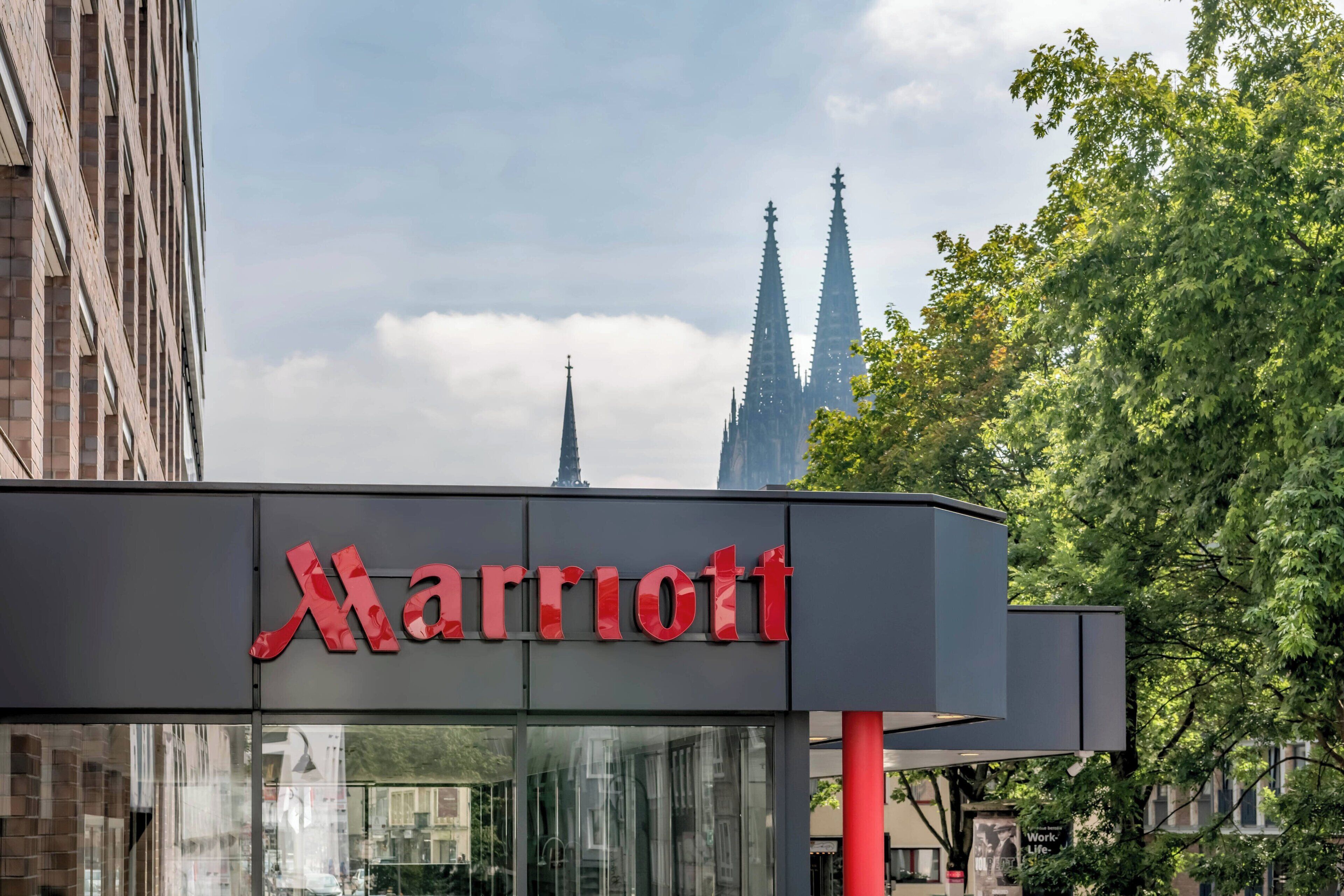 A Marriott hotel sign with a modern design, set against a backdrop of a cityscape and a church spire.