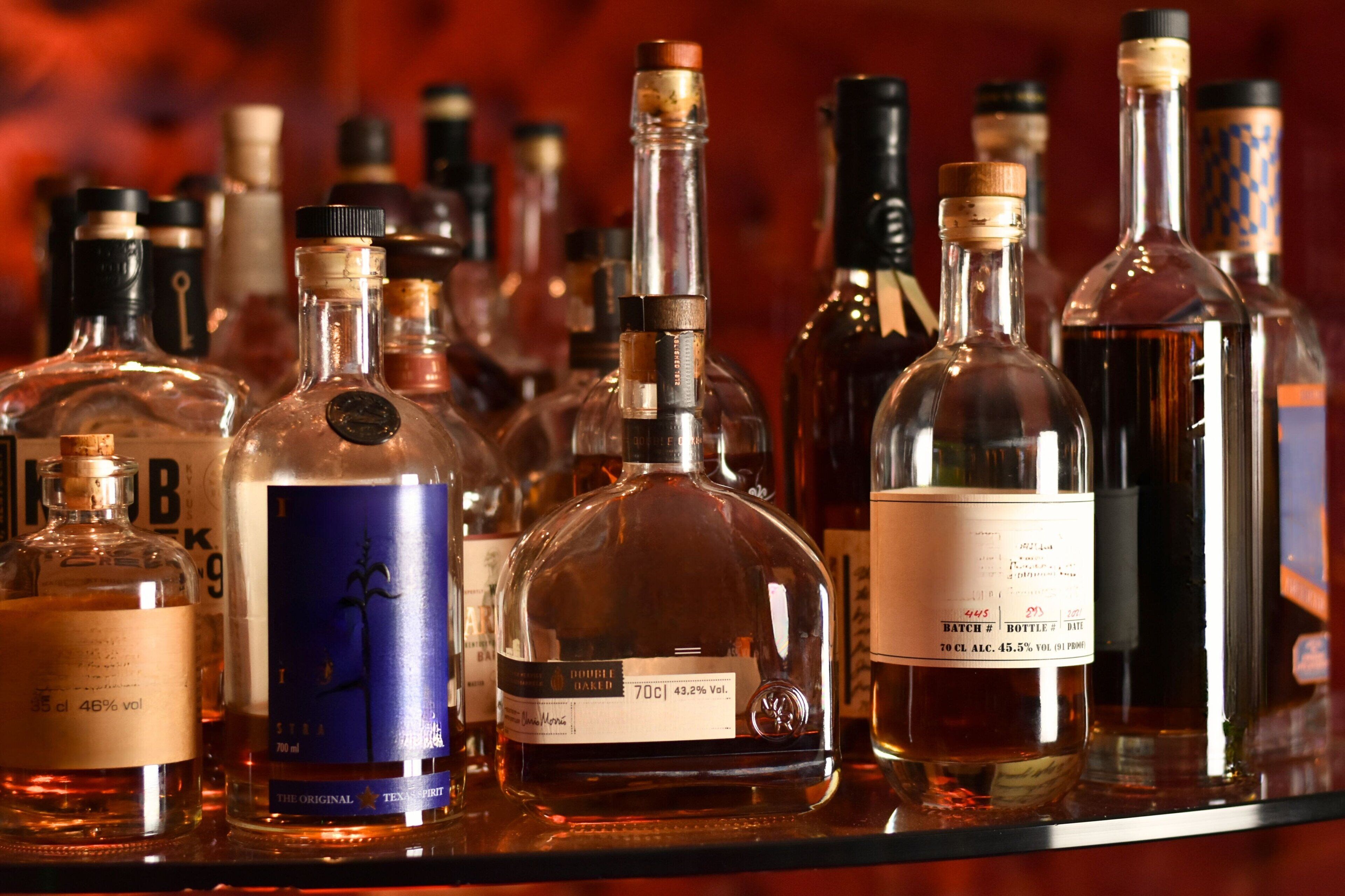 Diversas garrafas, provavelmente contendo bebidas alcoólicas, expostas numa prateleira.