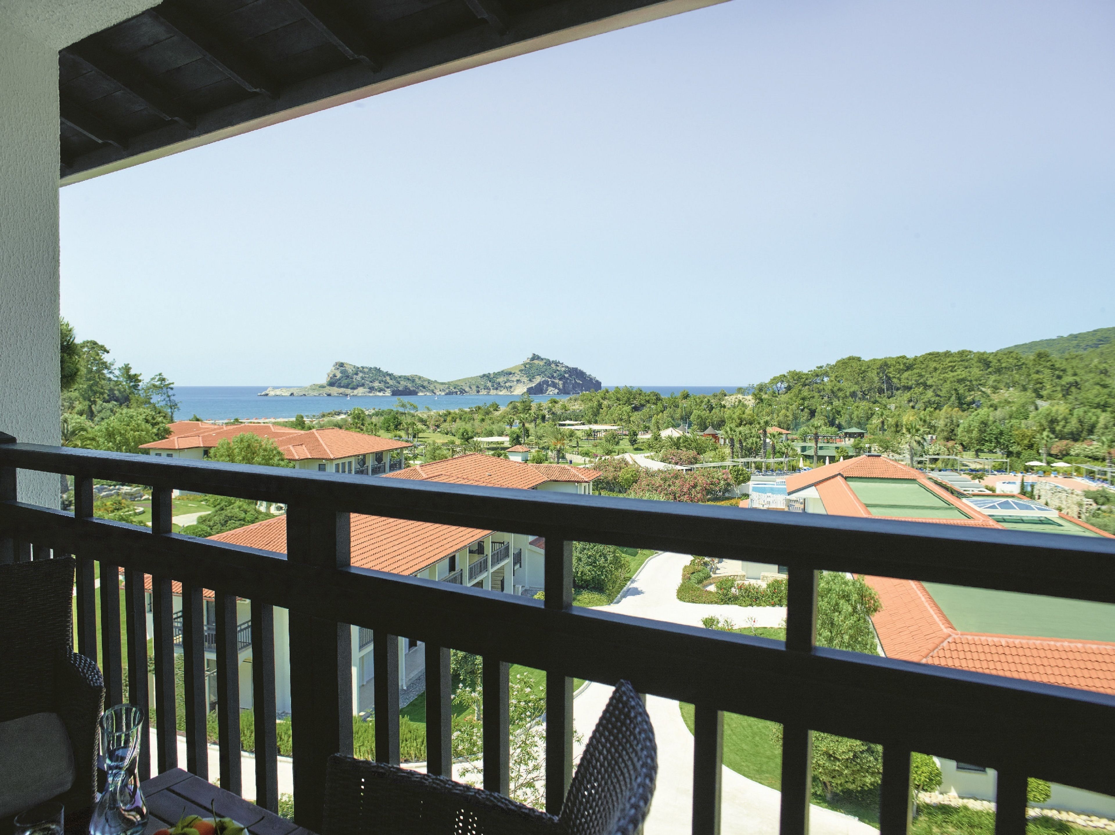 A balcony with a view of a coastal resort area, including buildings with red roofs and green spaces.