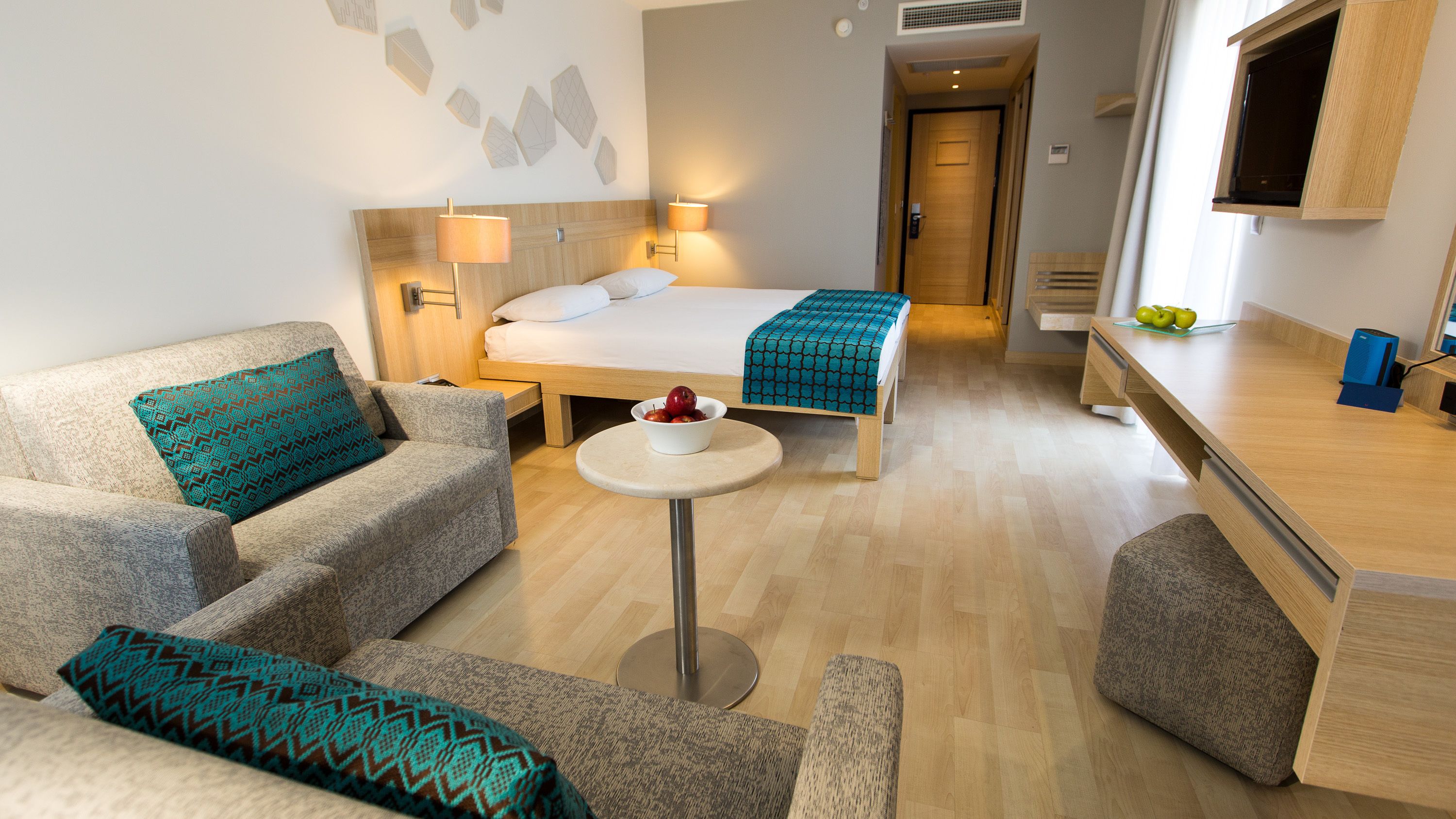 Una habitación de hotel moderna con sofá, una mesita redonda, cama con edredón estampado y escritorio con computadora.