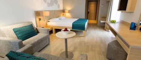 Una habitación de hotel moderna con sofá, una mesita redonda, cama con edredón estampado y escritorio con computadora.