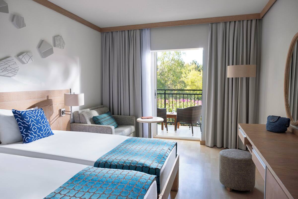 Ein Hotelzimmer mit einem großen Bett, einer Couch, einem kleinen Tisch und einem Balkon mit Vorhängen.