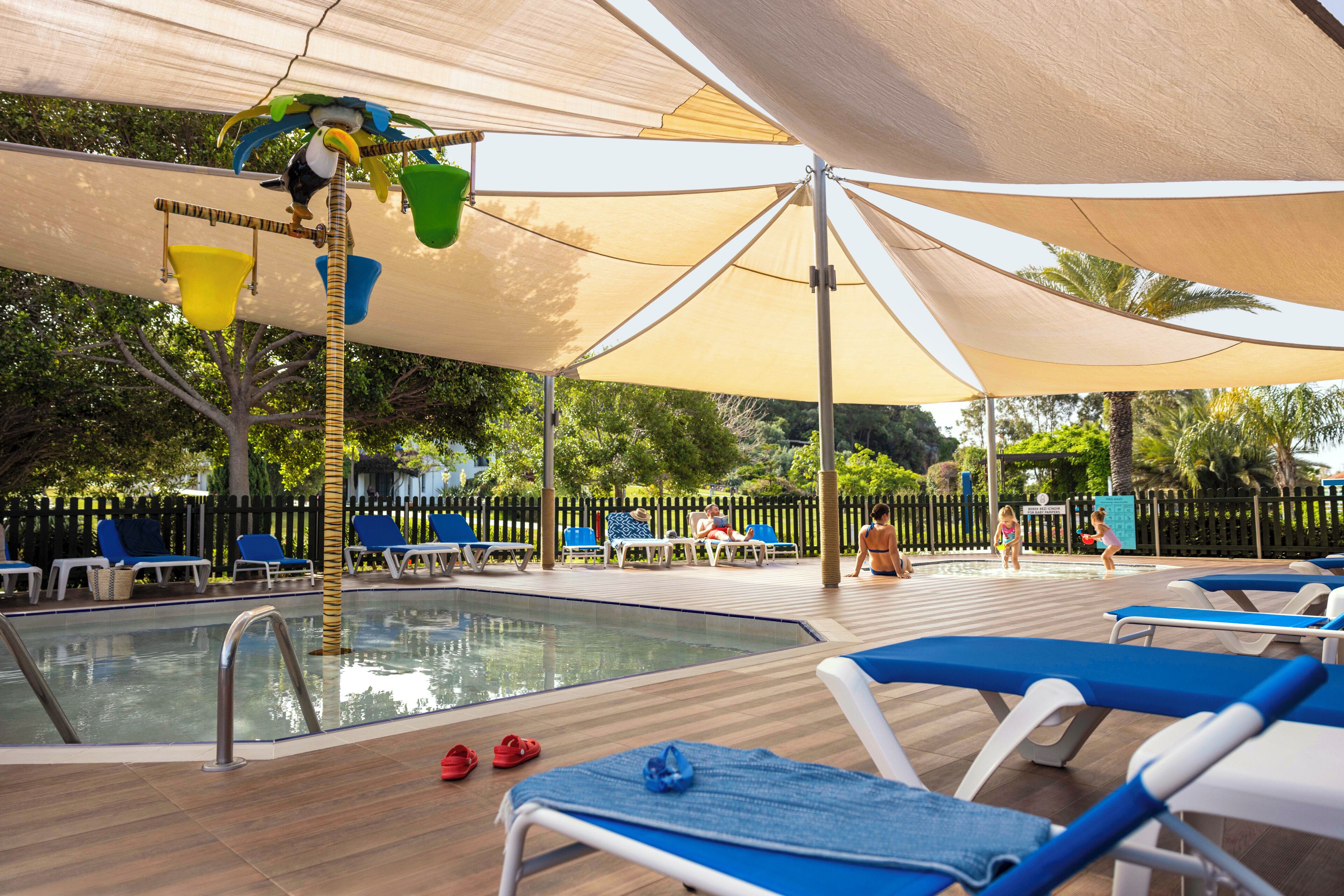 A poolside area with lounge chairs, a pool, and a shaded canopy.