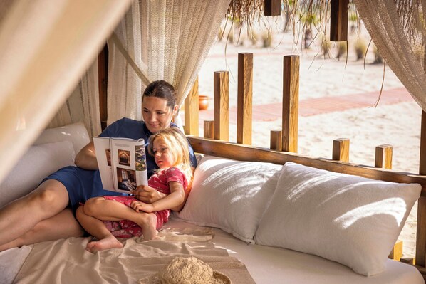 Una pareja en una cama con vistas a una playa arenosa.