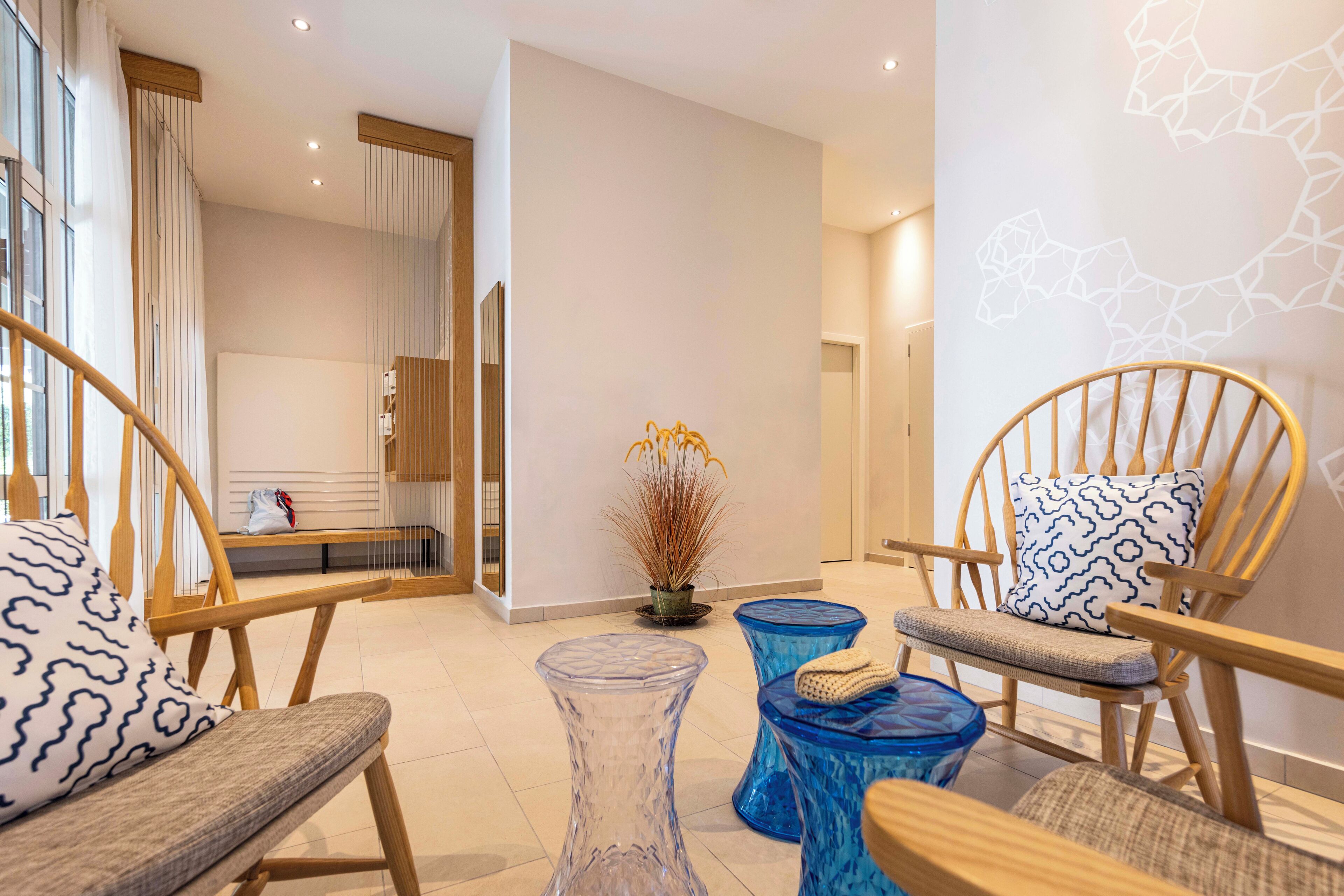 A modern hotel lobby with wooden chairs, a glass coffee table, and a blue ottoman.