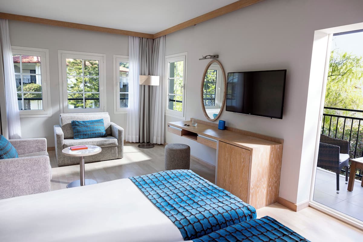 Ein Hotelzimmer mit Bett, Sofa, Schreibtisch, Fernseher und einem Balkon mit Gartenmöbeln.