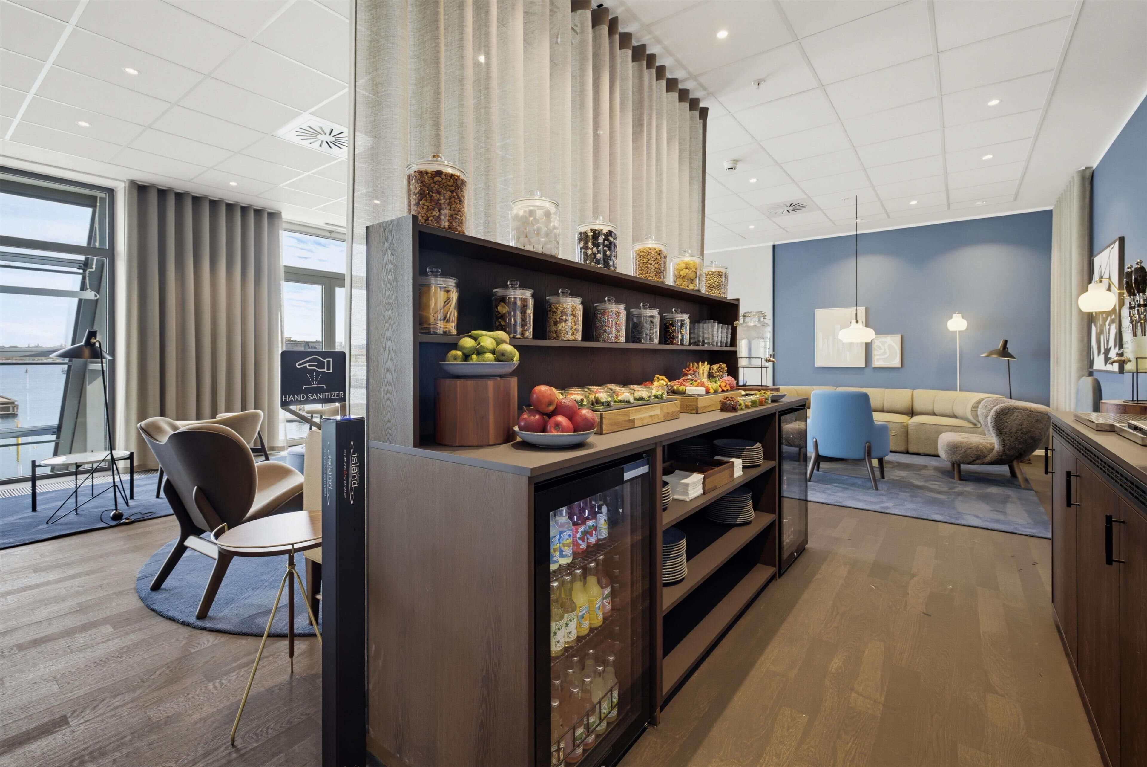 A modern hotel room with a kitchenette, a seating area, and a view of the city.