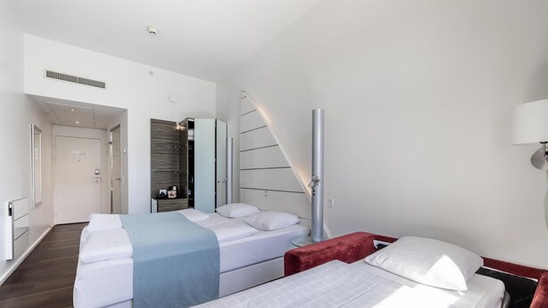 Habitación de hotel con dos camas, un armario, un espejo, una mesita de noche y una lámpara.