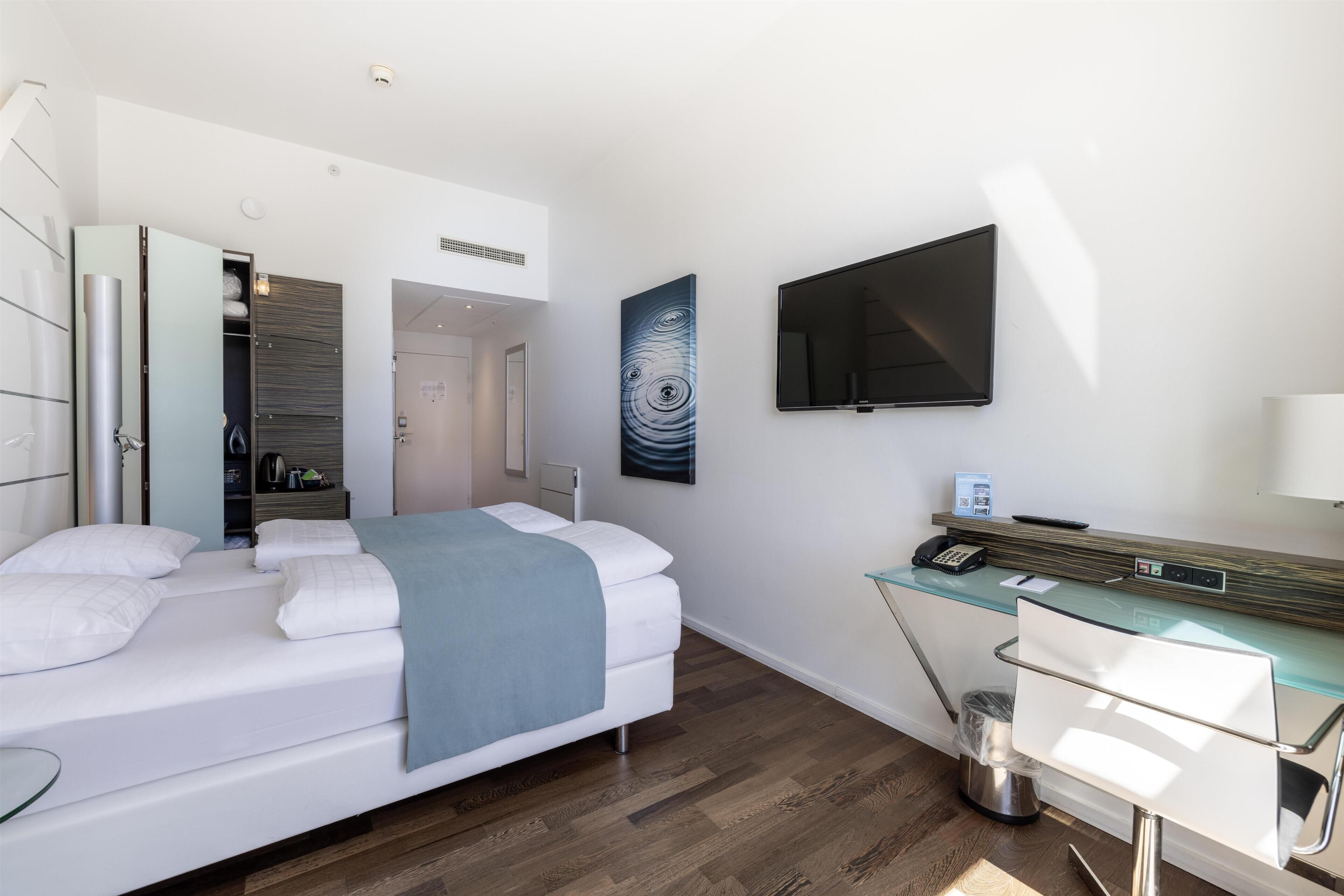 A hotel room with a bed, a desk with a computer, a TV, and a bathroom with a shower.