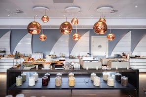 A modern kitchen with copper pendant lights, a buffet setup with various food items, and storage jars on the counter. - Copenhagen Island Hotel (Copenhagen)
