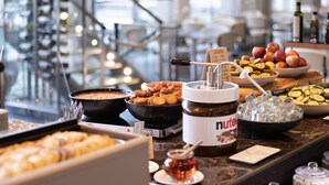 Un bufé con diversos alimentos, incluyendo un tazón de sopa, un recipiente con Nutella y una selección de frutas y verduras.