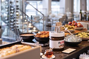 Un bufé con diversos alimentos, incluyendo un tazón de sopa, un recipiente con Nutella y una selección de frutas y verduras.