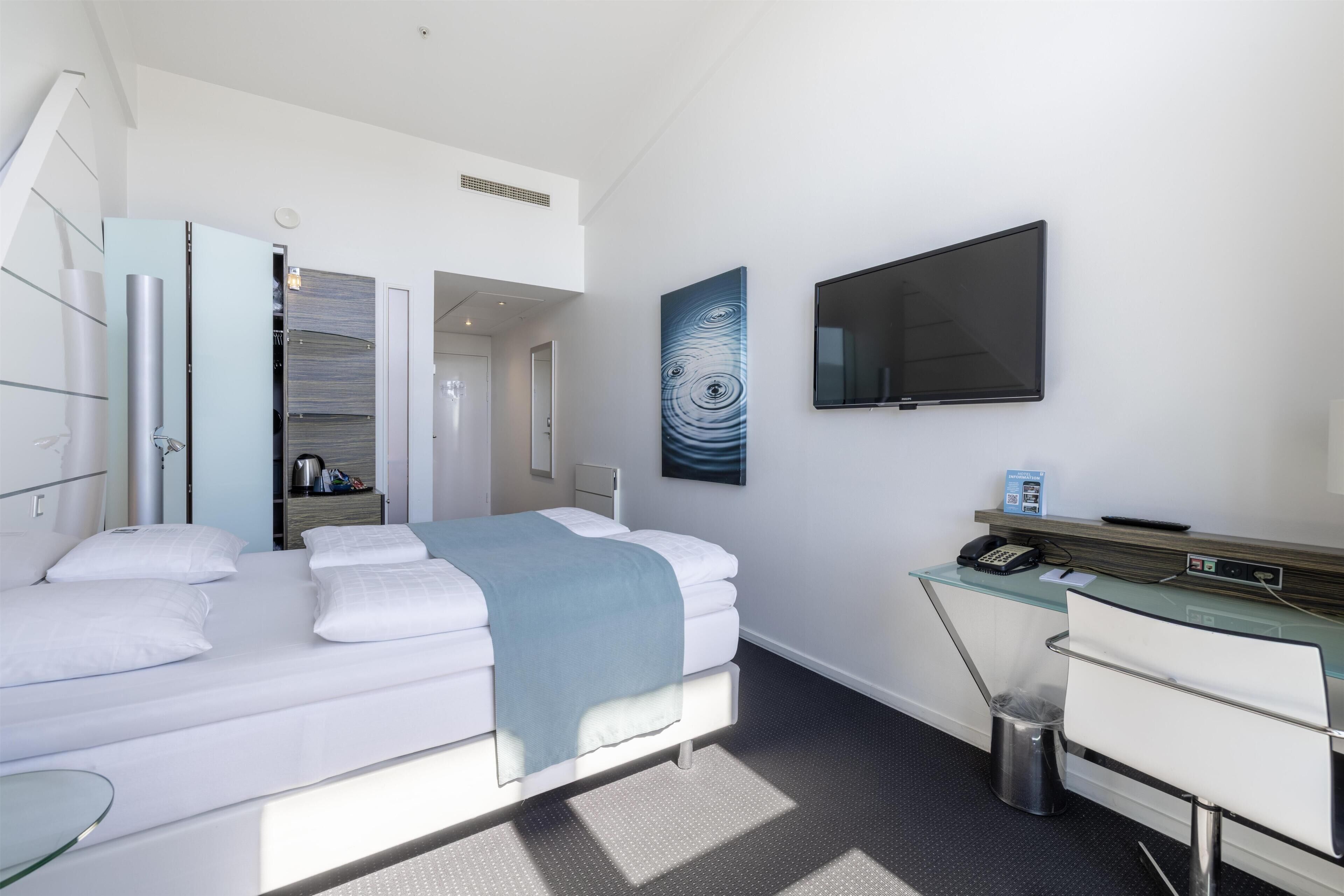 A modern hotel room with a bed, a desk, a TV, and a bathroom.