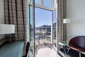 Een moderne hotelkamer met balkon, uitzicht op de haven en een zithoek met een tafel en stoelen.