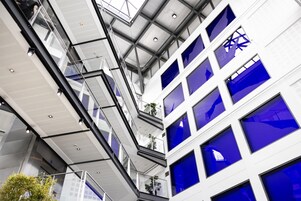 Un edificio de varios niveles con un diseño arquitectónico moderno, que presenta barandillas de vidrio y una serie de ventanas.