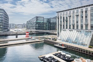 Een uitzicht op het water met moderne gebouwen, een steiger met boten en een heldere lucht.