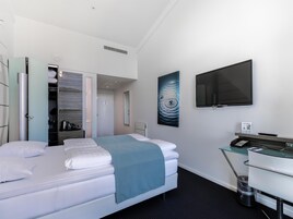 Una habitación de hotel con una cama, un escritorio con teléfono, un televisor de pantalla plana, un cuadro y un armario.