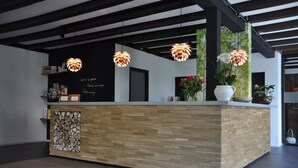 A reception area with a wooden reception desk, hanging pendant lights, and a wall with a chalkboard menu. - Hotel Bieze (Borger)
