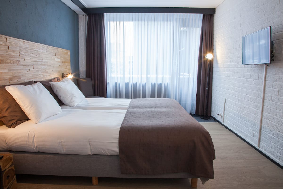 Moderni hotellihuone, jossa on suuri sänky, pääty, taulutelevisio ja suuri ikkuna, jossa on verhot.