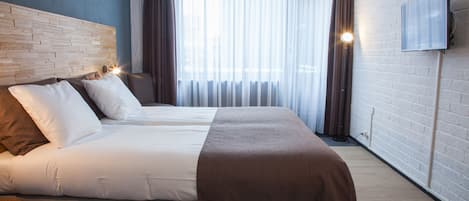Una habitación de hotel moderna con una cama grande, cabecero, televisor de pantalla plana y un ventanal con cortinas.