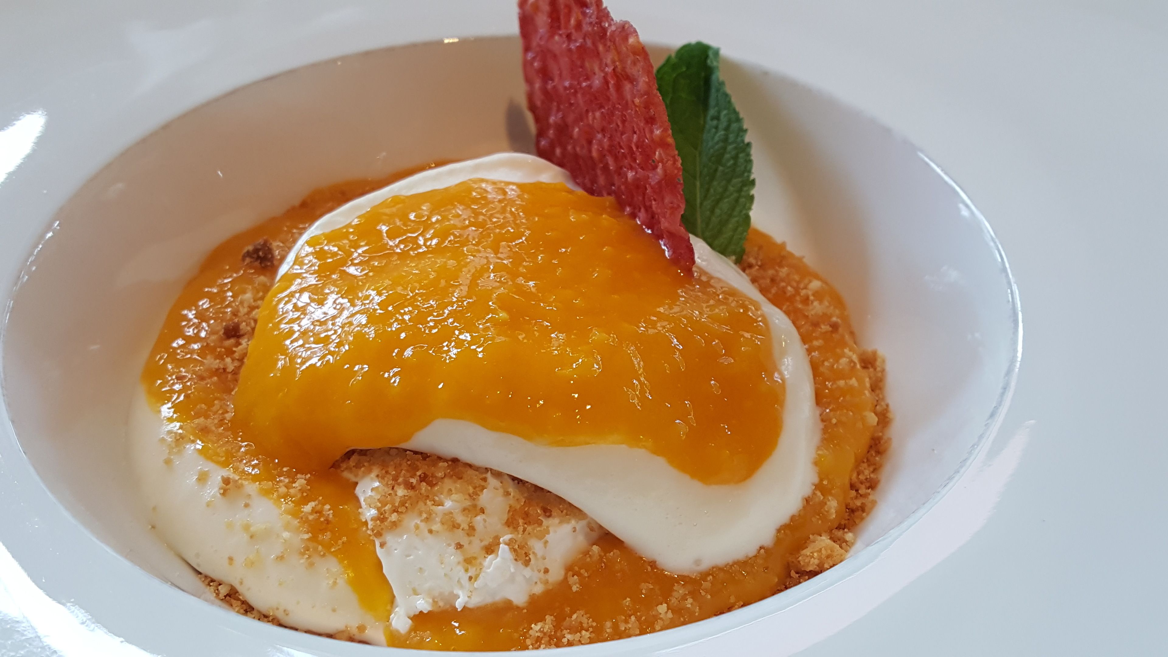 Dessert met een zachte basis, gegarneerd met een glanzende oranjesaus en kruimels, en een muntblaadje.