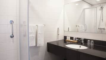 Een moderne badkamer met een douchecabine van glas, een zwart aanrechtblad met een wastafel en een grote spiegel.