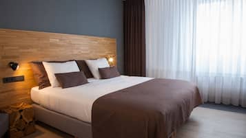 A neatly made bed with a wooden headboard, a bedside table with a lamp, and a window with sheer curtains.