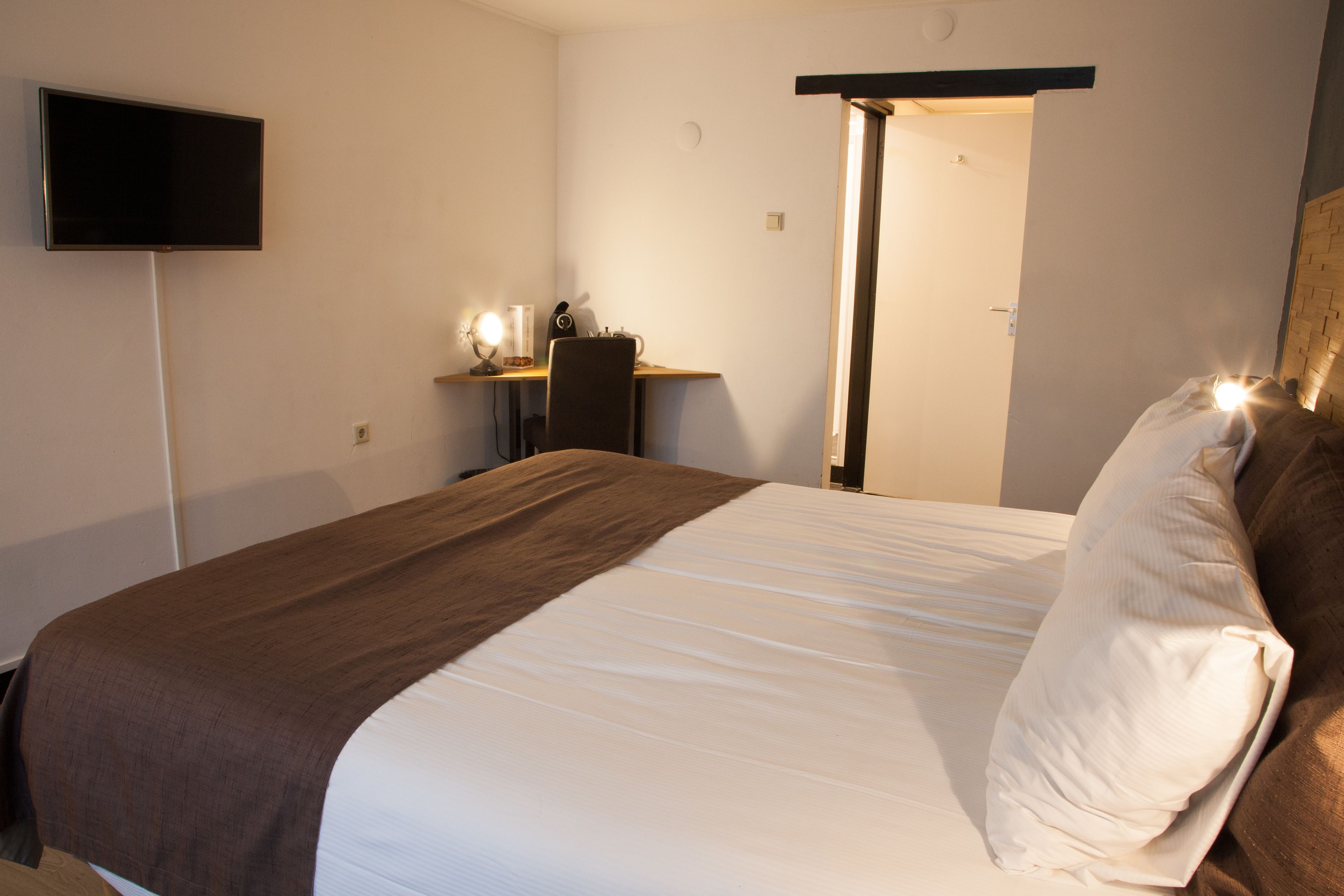Una habitación de hotel con una cama, un escritorio y un televisor montado en la pared.