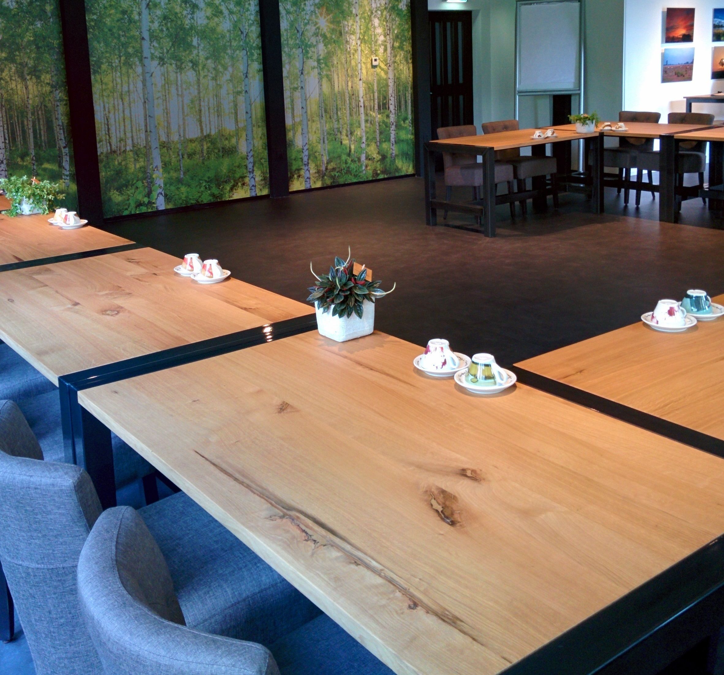 Sala de conferências com mesas compridas, cadeiras e um arranjo floral central.