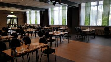 A conference room with multiple tables and chairs, large windows with curtains, and a brick wall with an emergency exit sign.