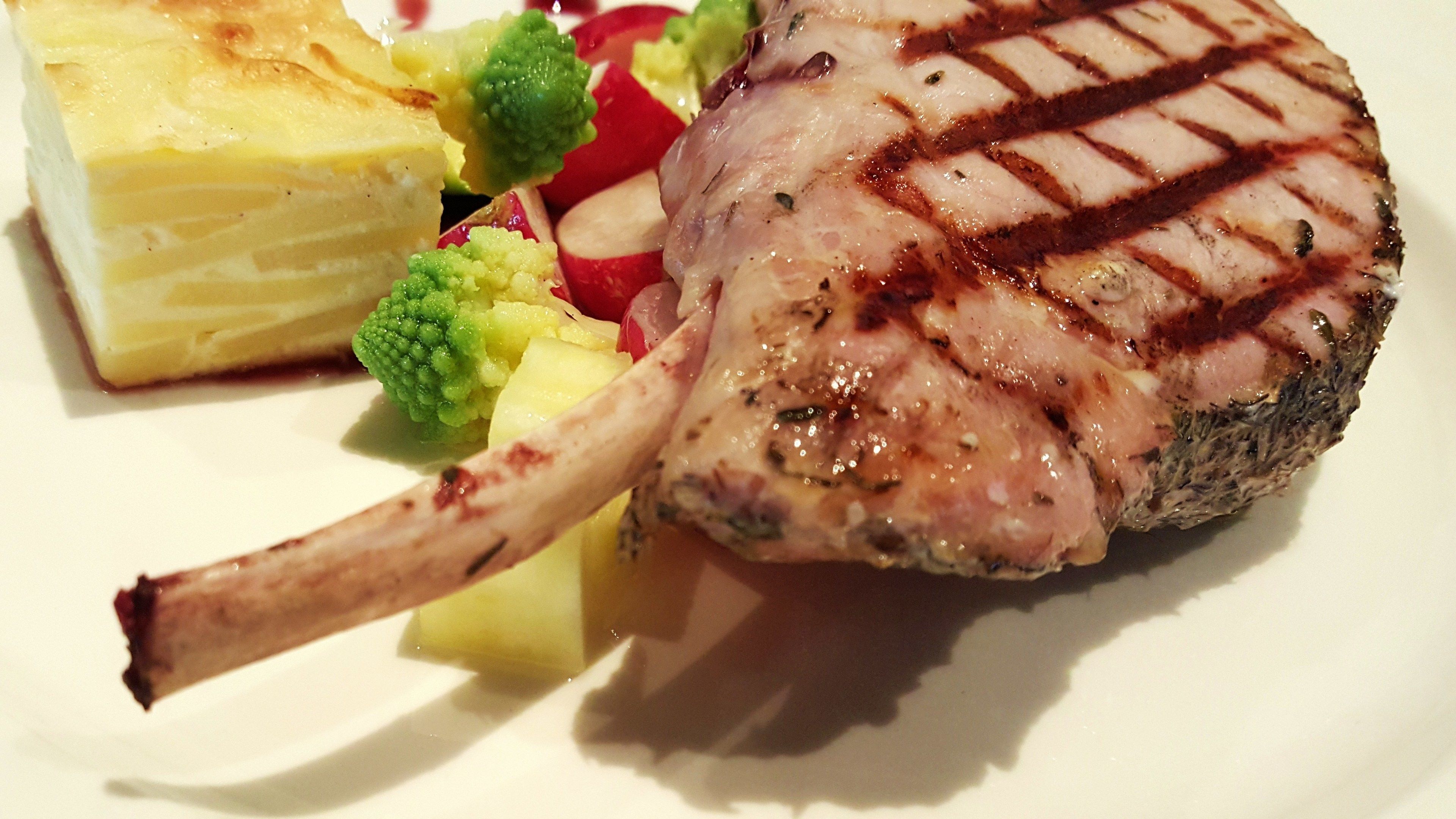 A grilled lamb chop with a side of mashed potatoes and steamed vegetables.