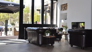 A modern interior with a leather sofa, a small table with a vase, and a fireplace. - Hotel Bieze (Borger)