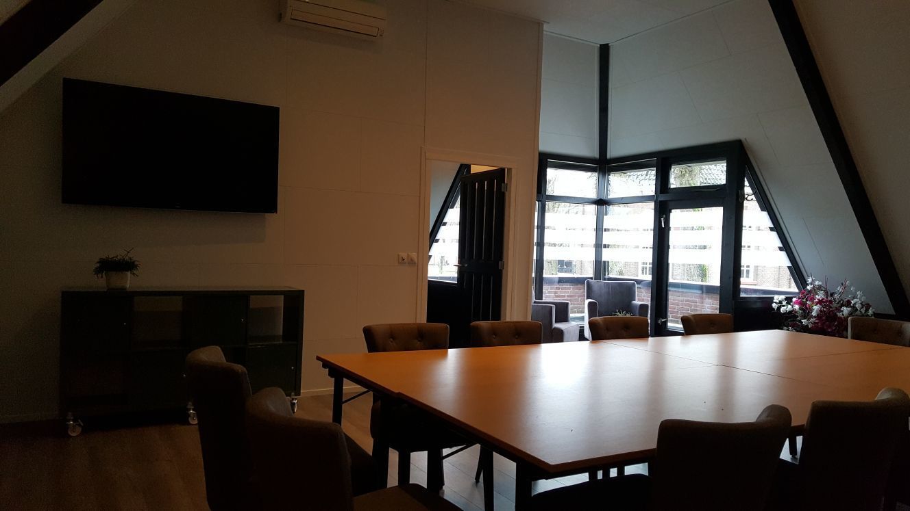 A conference room with a large table and chairs, a flat-screen TV mounted on the wall, and large windows with a view of the outside.