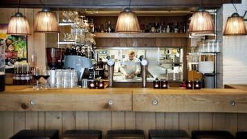 A bar area with wooden counters, hanging lamps, and a bartender preparing drinks.