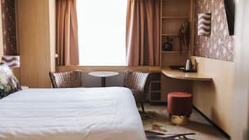 Una camera d'albergo con un letto, due poltrone, un tavolino, un comodino, una pianta e una parete decorata.