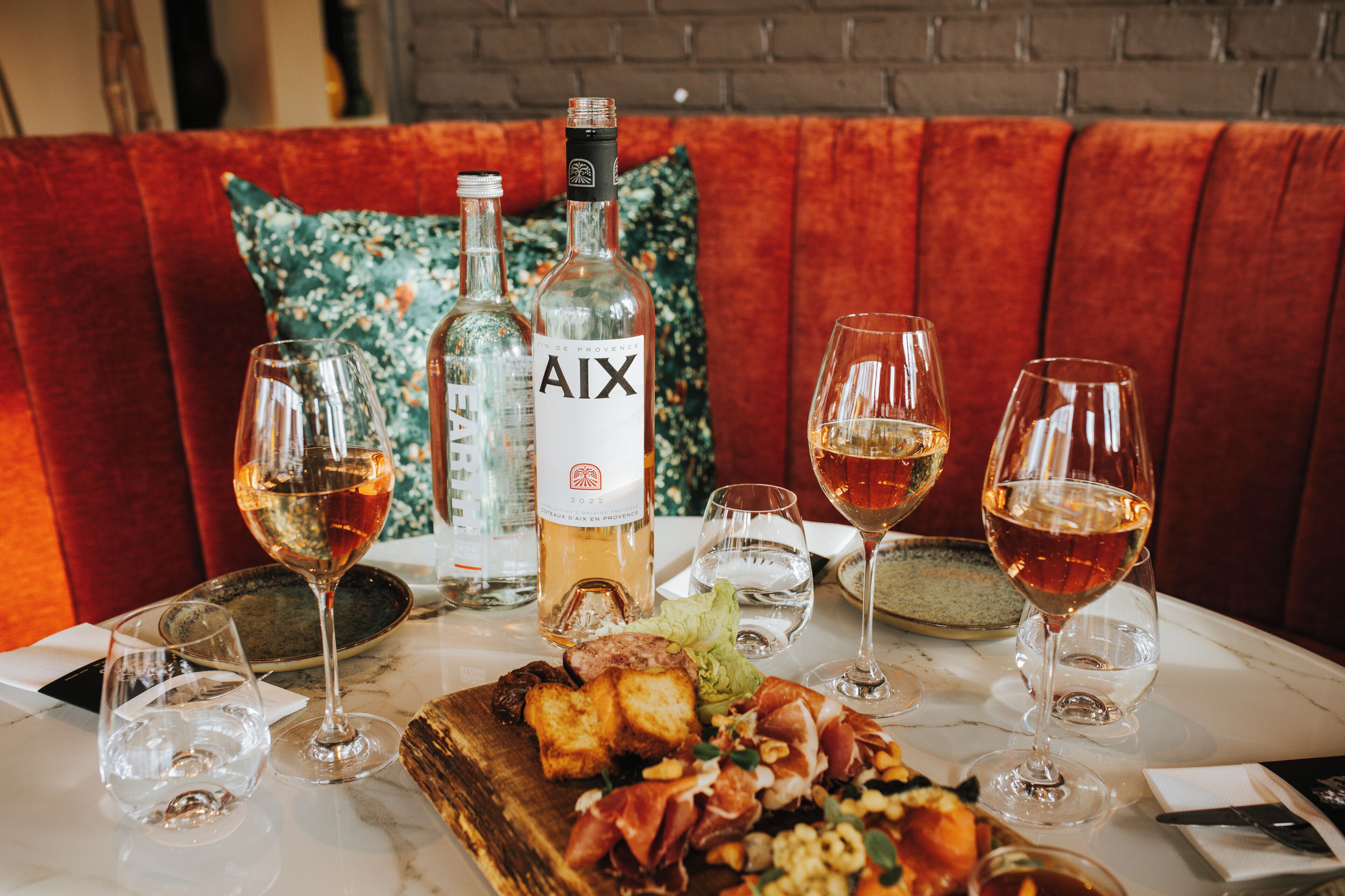 Een eettafel met wijnglazen, een fles AIX wijn en een houten plank met eten.