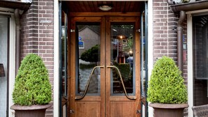 A hotel café restaurant entrance with a wooden door, a sign above it, and two potted plants on either side. - Hotel en Restaurant Wesseling (Dwingeloo)