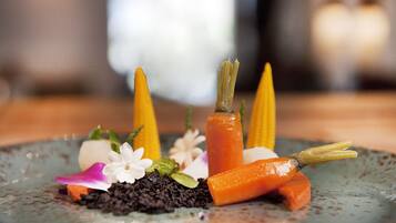Um prato com base escura, coberto por uma cenoura, um sabugo de milho e algumas flores brancas.