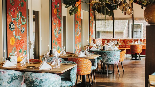 A restaurant interior with floral wall art, wooden tables, and colorful chairs. - Hotel en Restaurant Wesseling (Dwingeloo)