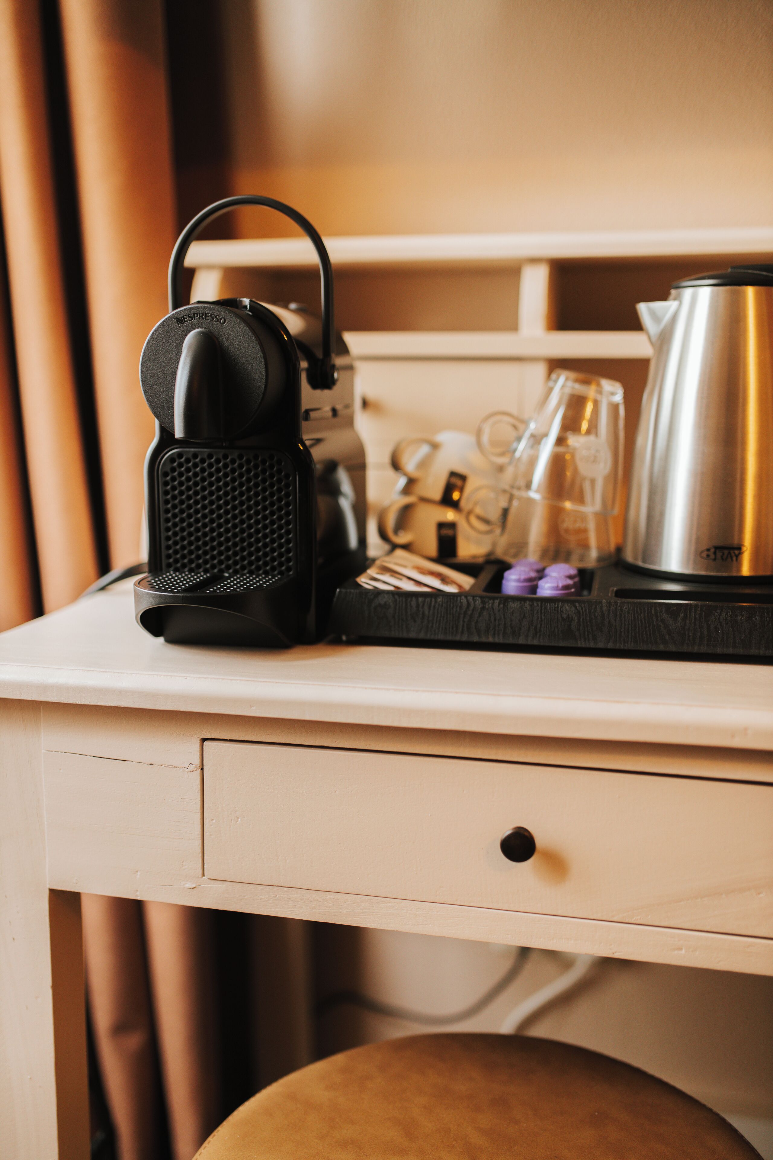 A kitchenette with a coffee maker, a kettle, and a tray with glasses and a bottle.