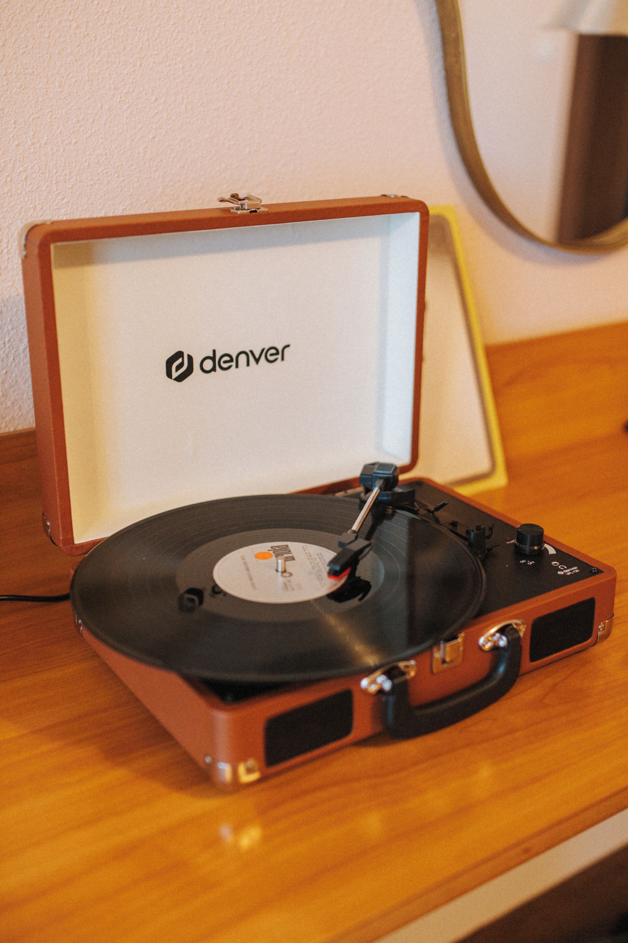 Um toca-discos com o logotipo Denver na capa, sobre uma superfície de madeira.