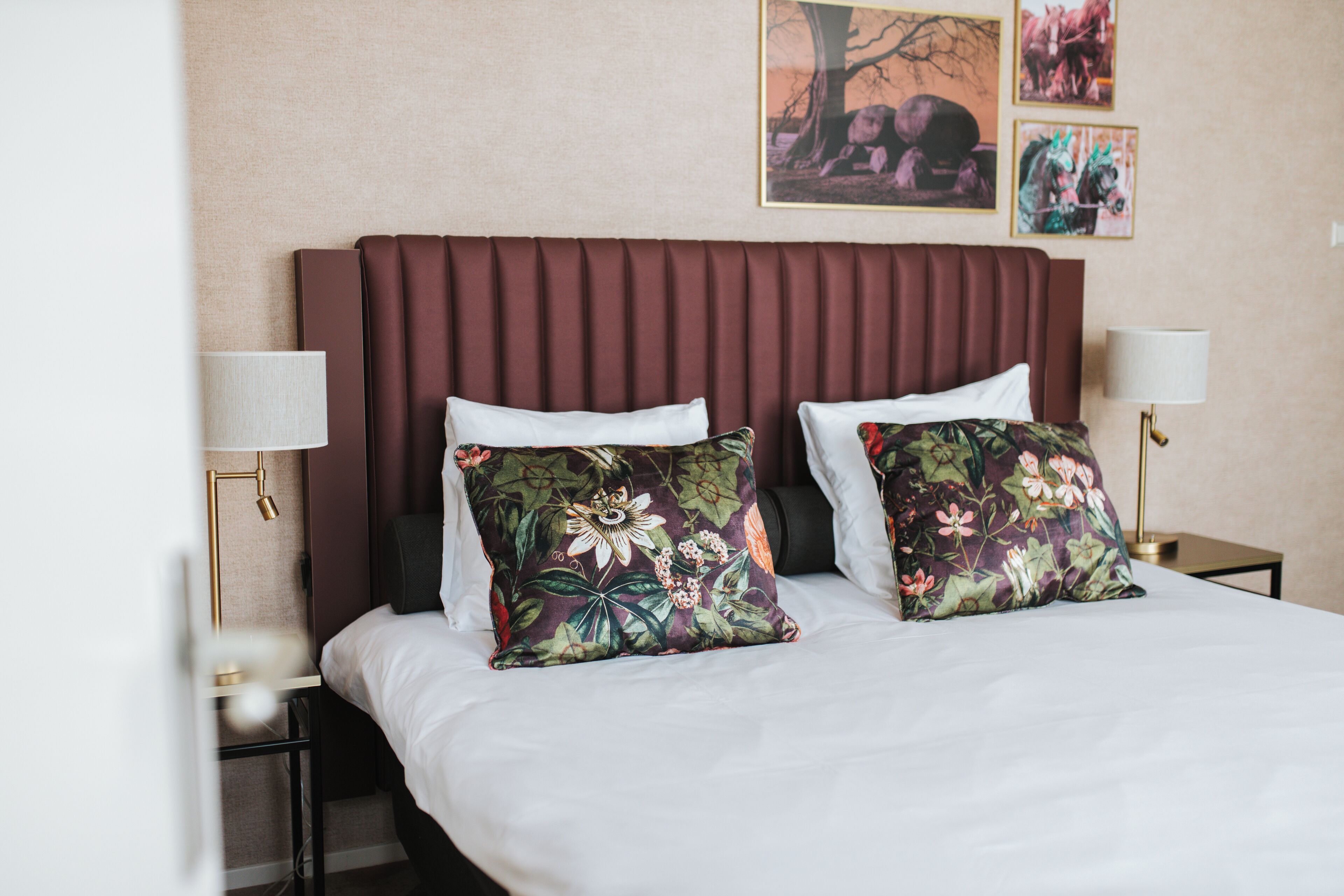 A hotel room with a large bed, two side tables with lamps, and floral-patterned pillows.