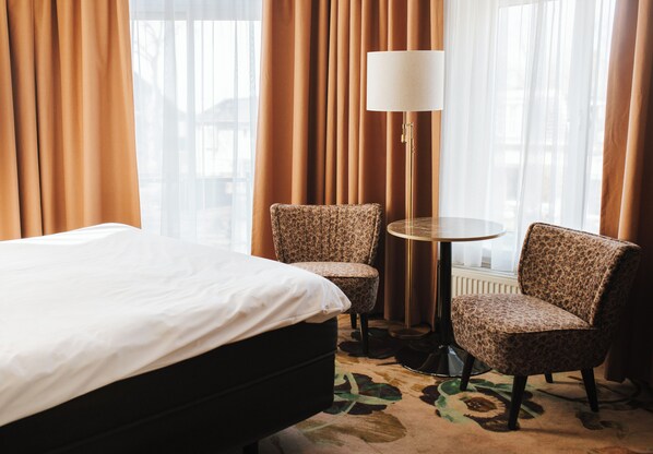 Una habitación de hotel con una cama, dos sillas, una mesa y una lámpara.