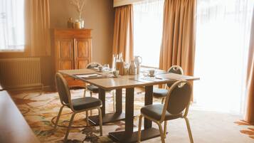 A dining area with a table set for four, surrounded by chairs. A wooden cabinet is against the wall, and a radiator is visible to the left.