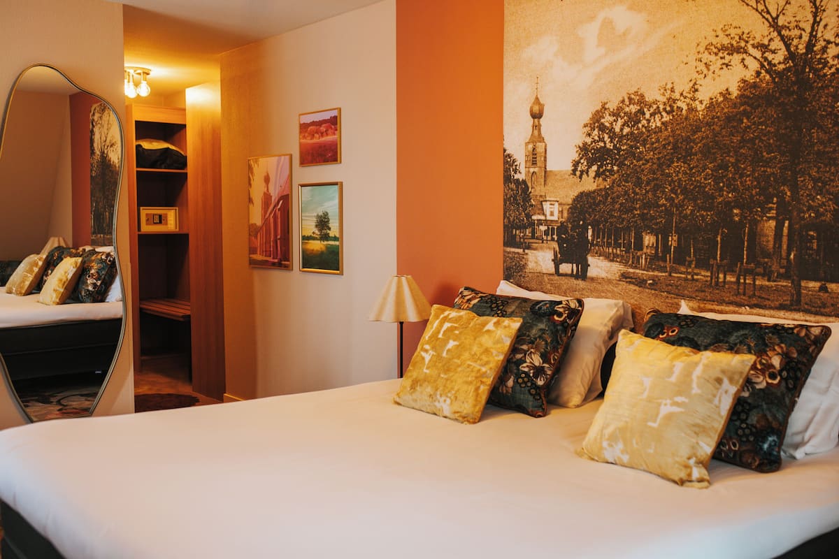 Una habitación de hotel con una cama, un espejo, una lámpara y un tapiz grande en la pared.