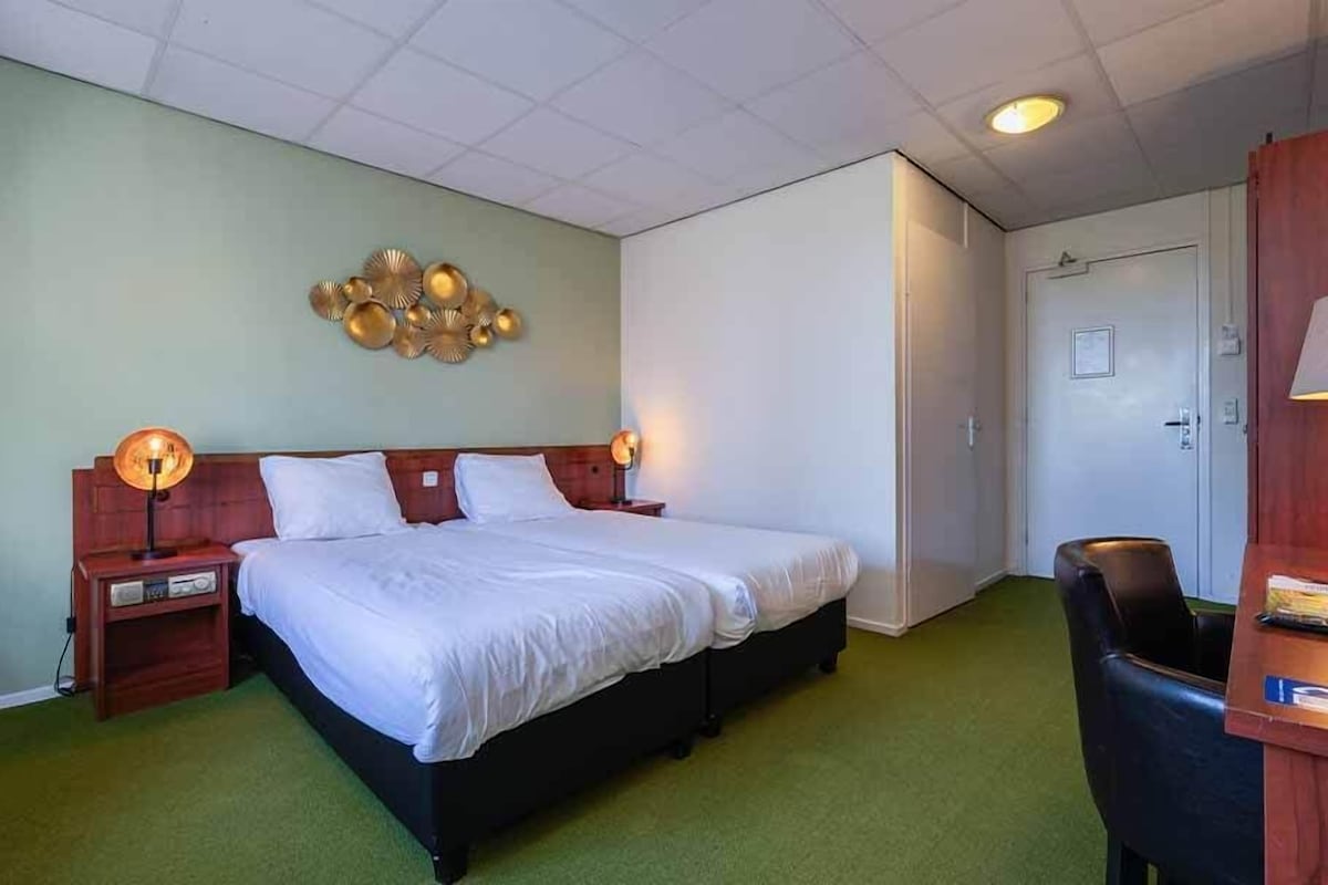 Una habitación de hotel con una cama, mesitas de noche, un escritorio y una silla.