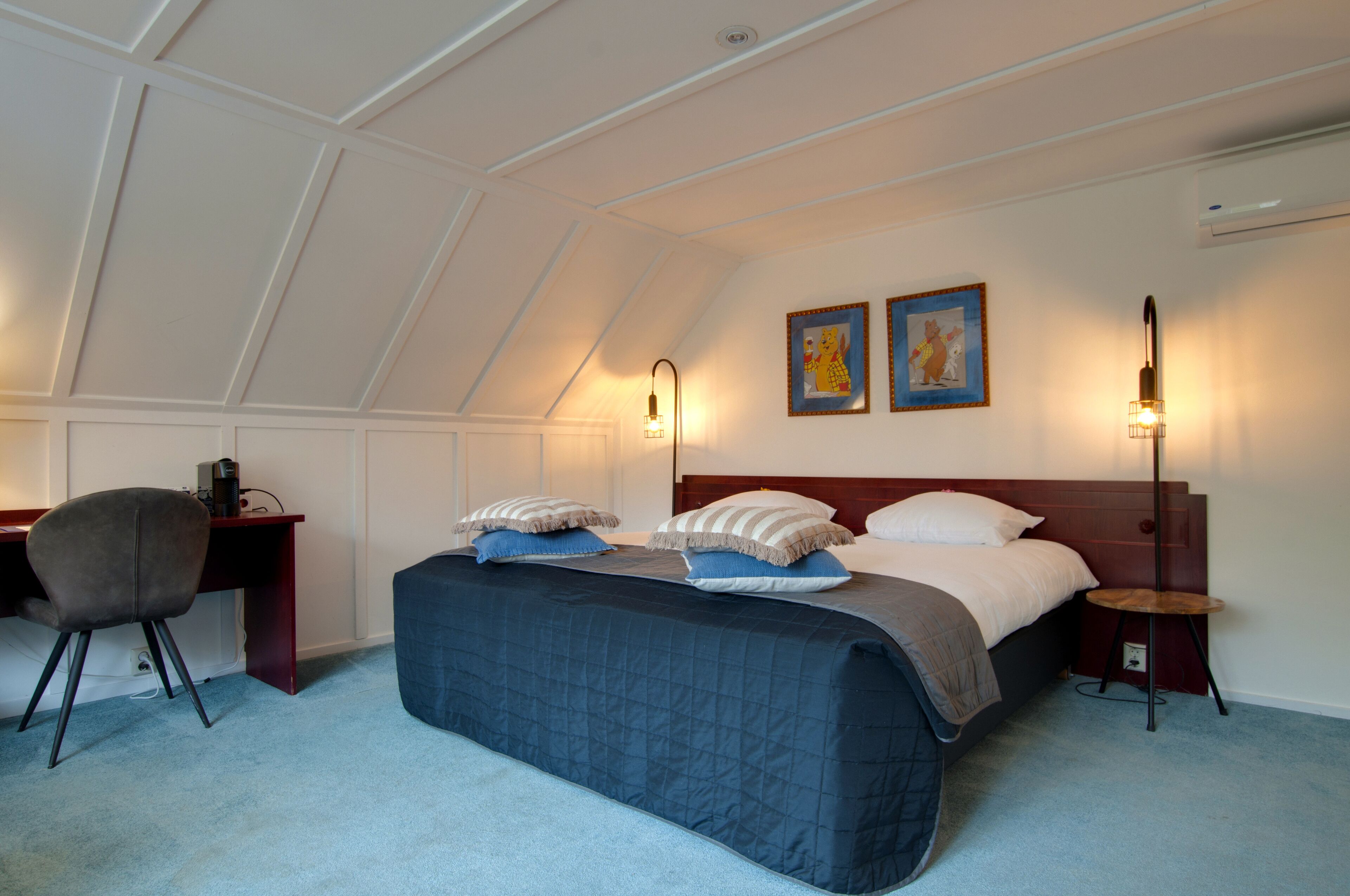 A bedroom with a bed, desk, chair, and two wall-mounted lamps.